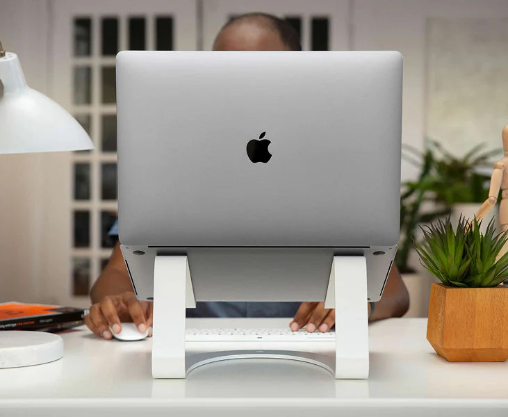 Person using a laptop on a white stand with an Apple logo in a home office setting.